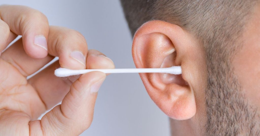 Adult about to clean ear with a cotton bud, illustrating ear cleaning safety concerns