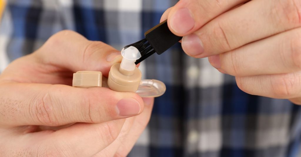 Person cleaning a hearing aid as part of routine maintenance